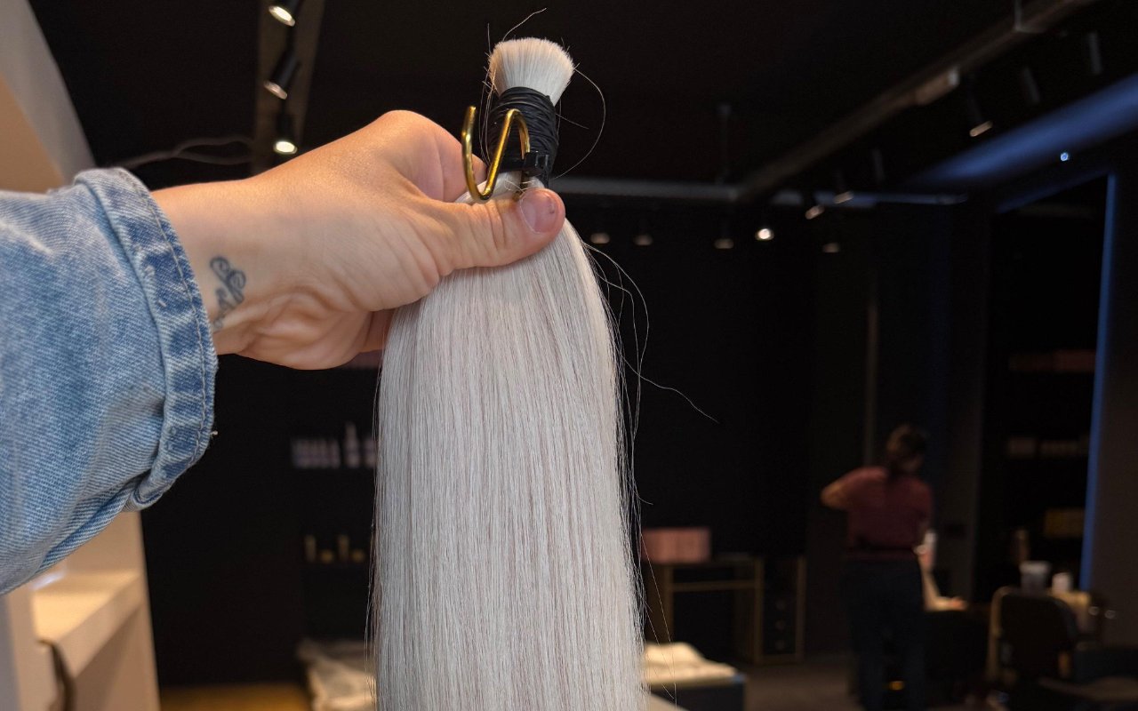 Een bundel zilverblonde extensions in de hand, in de salon