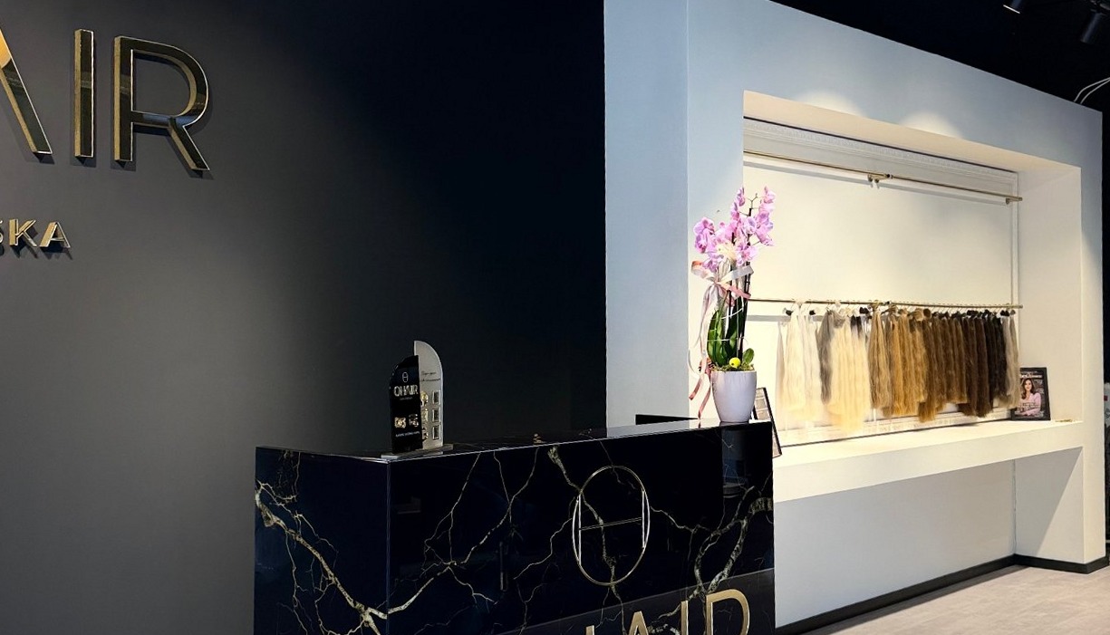 De balie van zwart marmer met gouden aders, het OHAIR-logo op de muur en de witte wand met extensions in alle kleuren